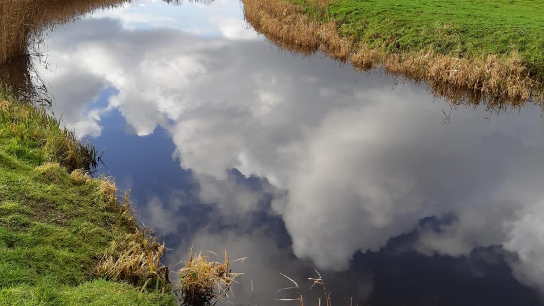 Een sloot in Heiloo met wolkenlucht daarin gespiegeld