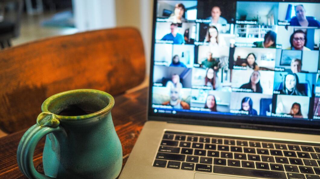 een beeldscherm met online vergaderaars en een kopje koffie