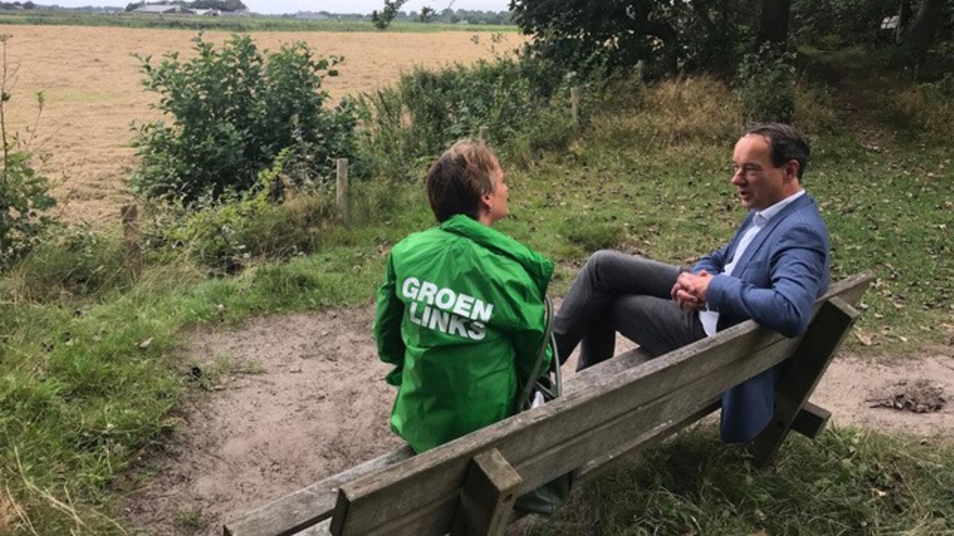 Een groenlinkser praat op een bankje in het bos met een man in een pak